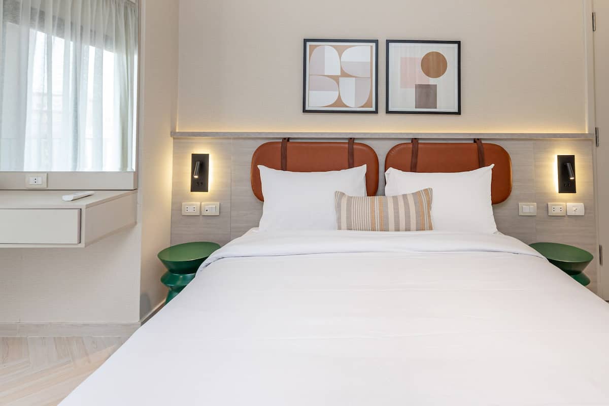 A hotel room with a large bed, two nightstands, a bedside table, a mirror, and two framed abstract artworks on the wall.