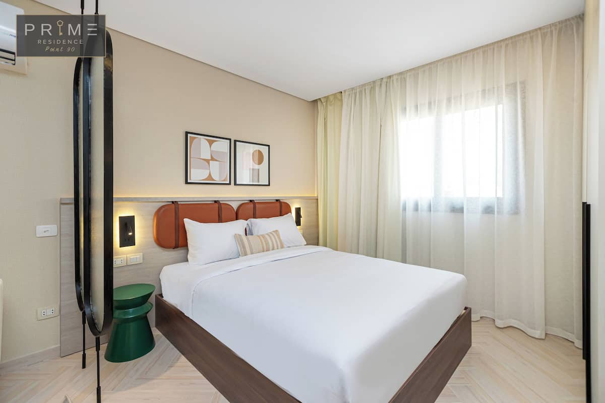 A modern hotel room with a large bed, a green side table, and a wall-mounted TV.