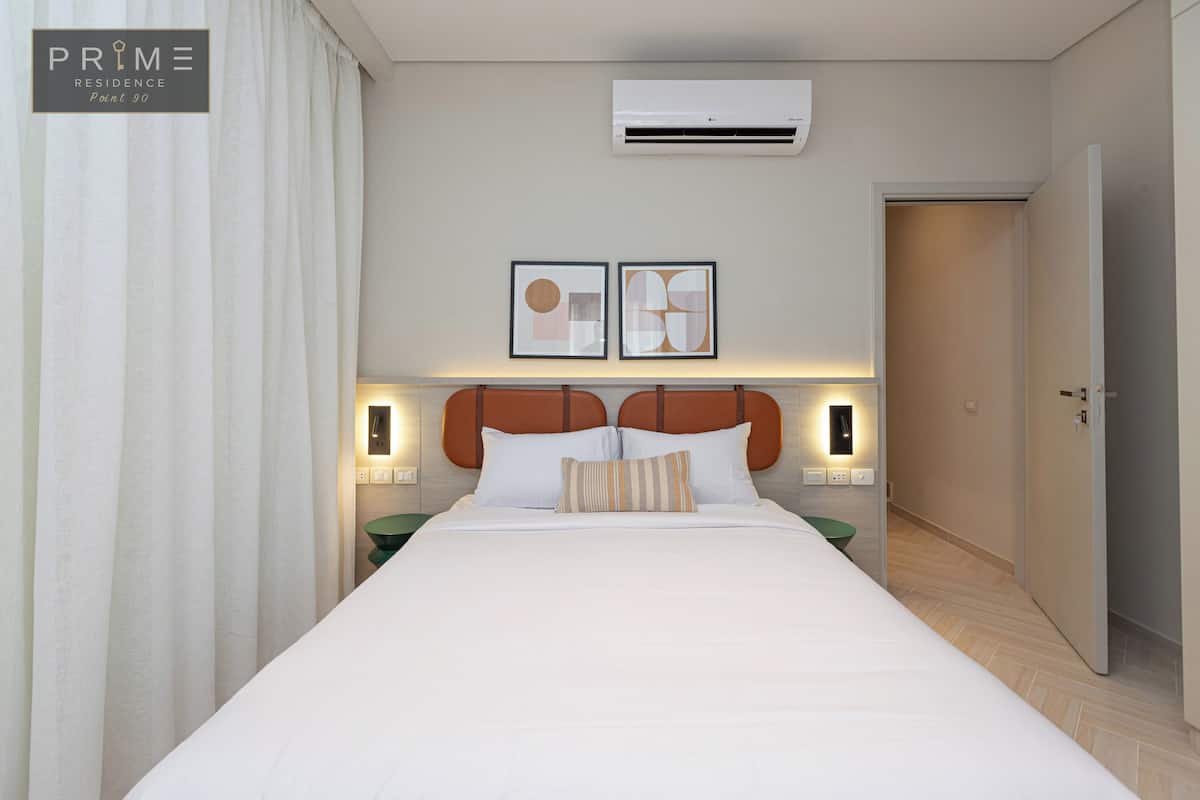 A hotel room with a large bed, a headboard with a circular design, two wall-mounted lights, and a framed picture above the bed.
