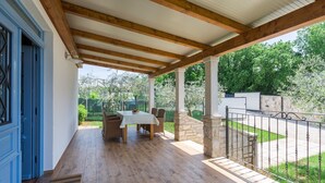 A covered patio with a table and chairs, a wooden floor, and a stone wall.