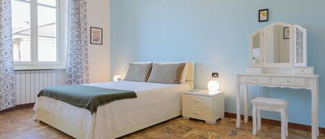 Ein Schlafzimmer mit Bett, Nachttischen, einem Schminktisch und einem Fenster mit Vorhängen.