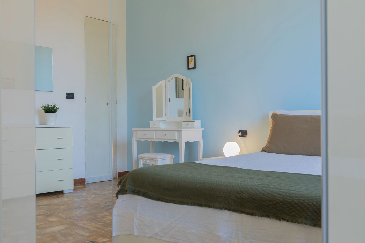 Une chambre à coucher comprenant un lit, une commode, une coiffeuse avec un miroir et une lampe de chevet.