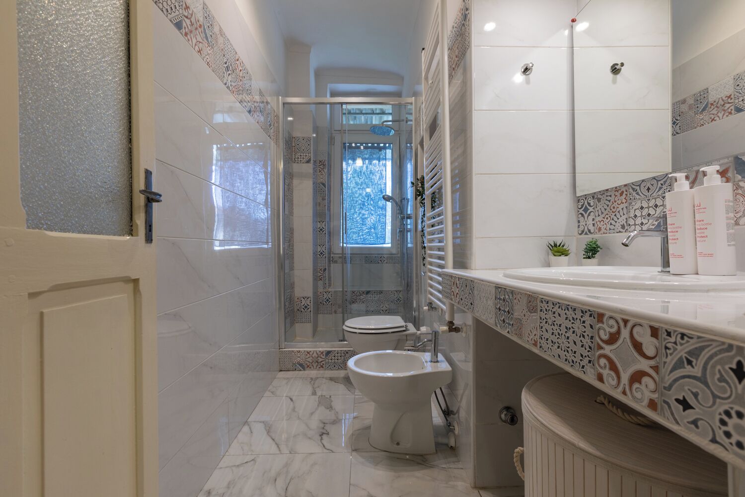 A modern bathroom with a glass-enclosed shower, a toilet, and a sink with decorative tiles.