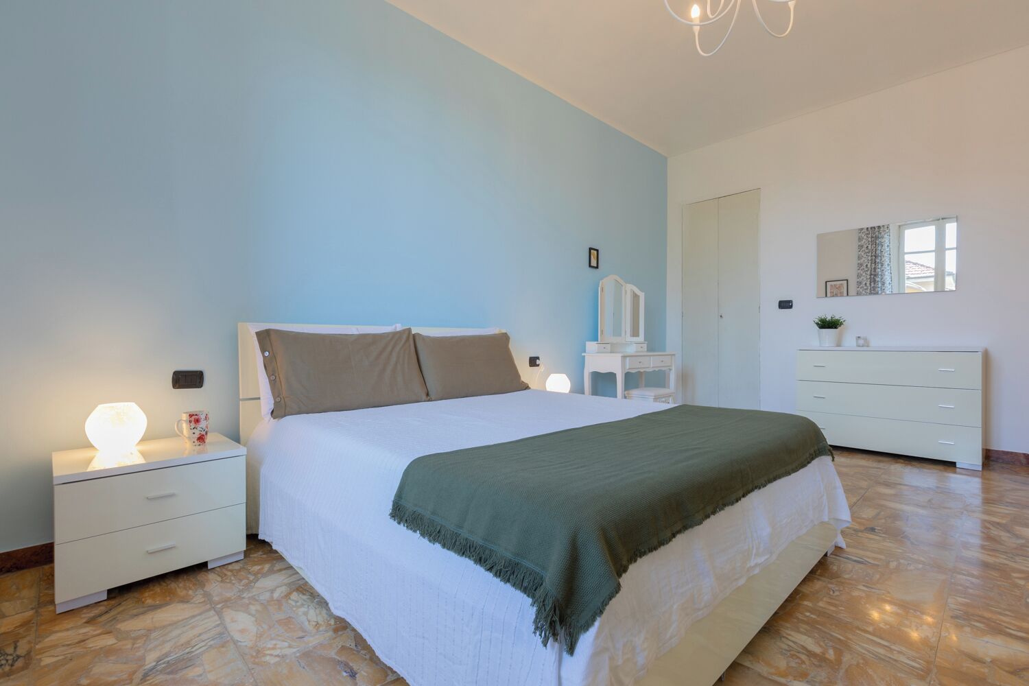 Um quarto com cama, mesas de cabeceira, cômoda e espelho.