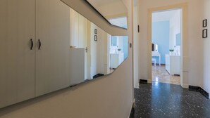 A modern hallway with white walls and a black marble floor. There are white cabinets with dark handles on the left, and a white door at the end. - The Turin Nest by Wonderful Italy (Turin)
