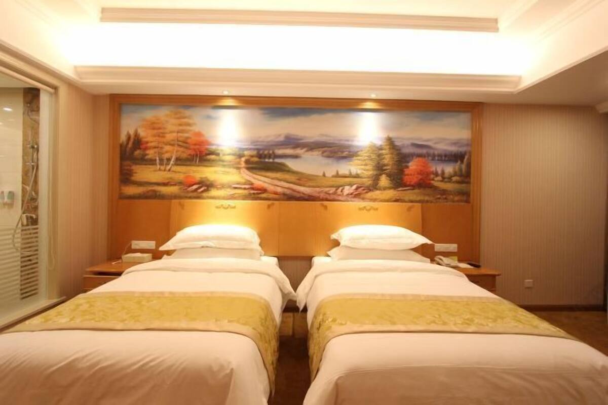 Une chambre d’hôtel avec deux lits, un tableau représentant un paysage accroché au mur et une fenêtre avec des stores.