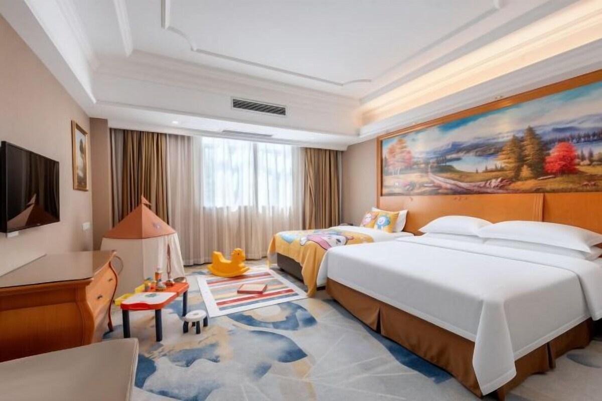 A hotel room with a bed, a desk, a chair, a television, and a painting on the wall.