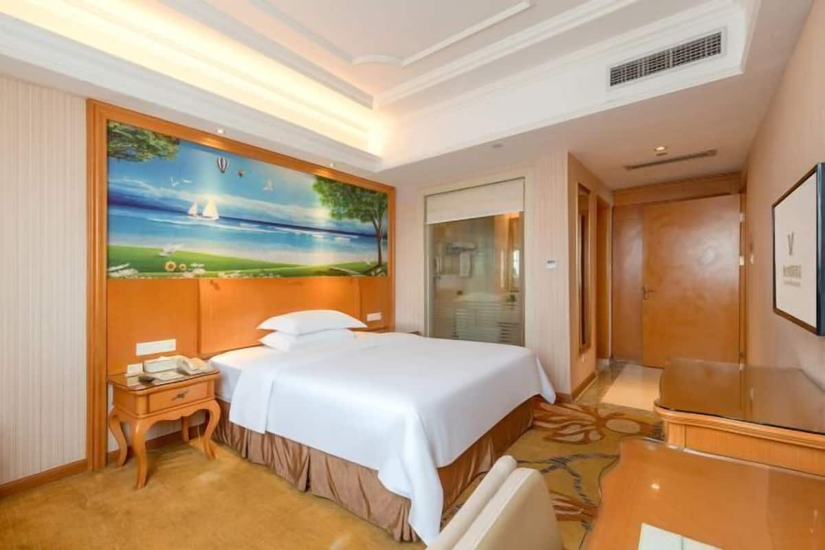Une chambre d’hôtel avec un grand lit, une table de chevet, un tableau représentant un paysage, une porte vitrée et un téléviseur.