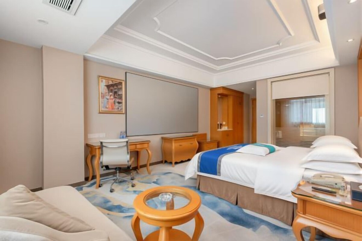 A hotel room with a bed, desk, chair, and a large window.