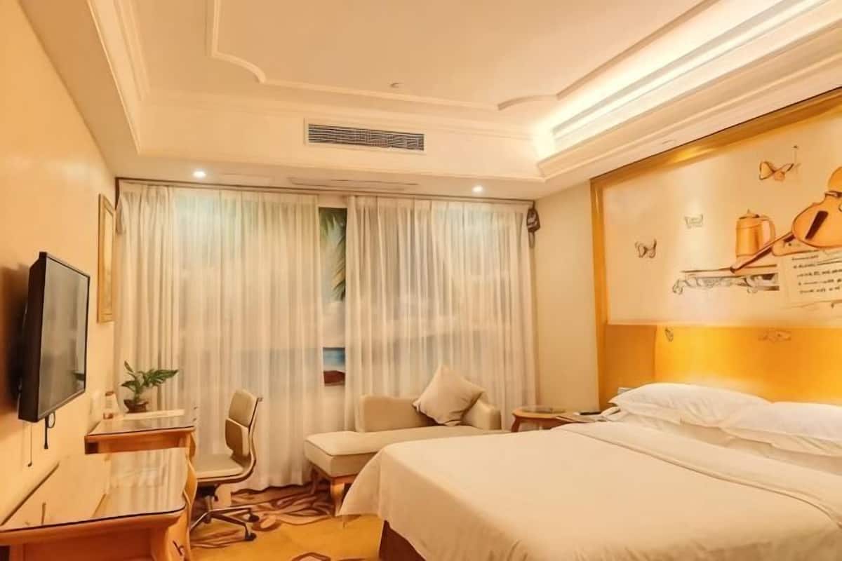 Une chambre d’hôtel avec un lit, un bureau, une chaise, une télévision et des rideaux.