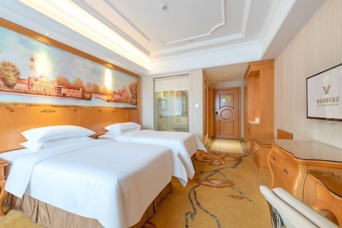 Une chambre d’hôtel avec deux lits, un tableau au mur, un bureau et un miroir.