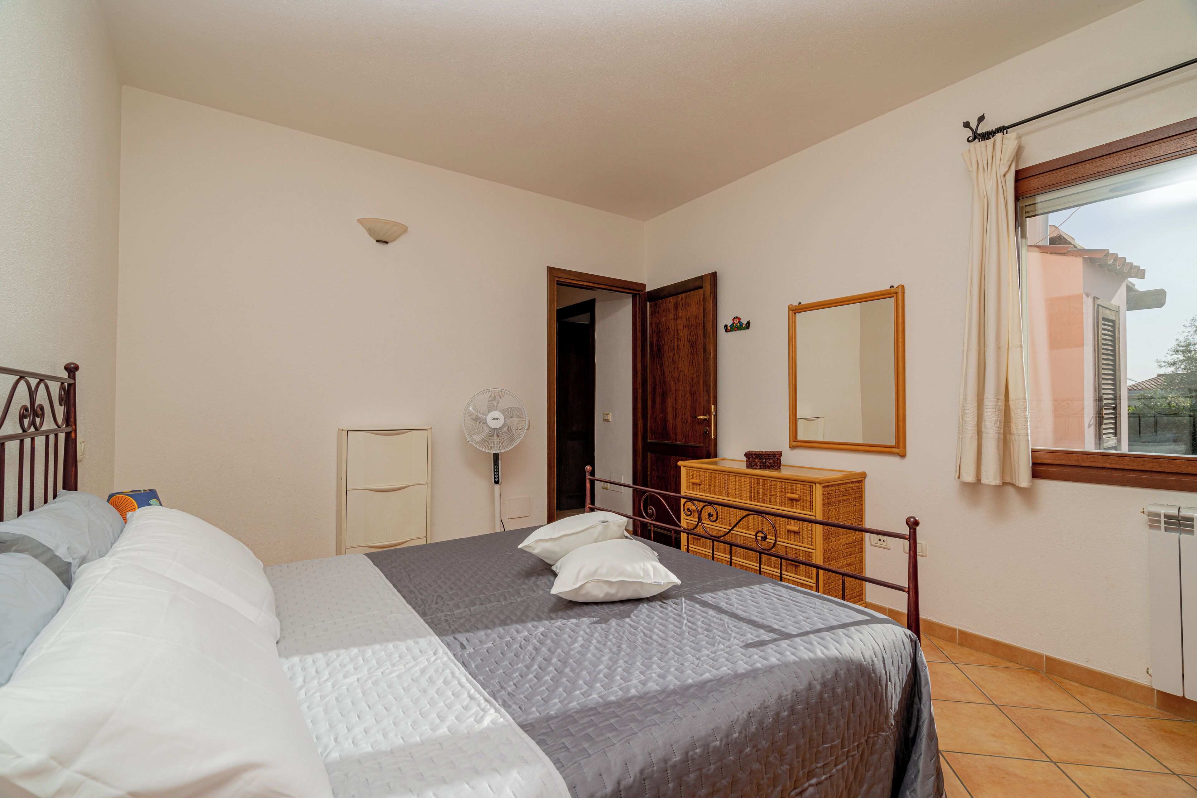 A bedroom with a bed, dresser, mirror, and a window with curtains.
