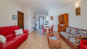 A living room with a red sofa, a wicker sofa, a dining table with chairs, and a kitchen in the background. - Casa Helen by Wonderful Italy (Olbia)