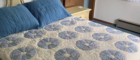 A bed with a floral quilt, a wooden wardrobe, and a white air conditioner.