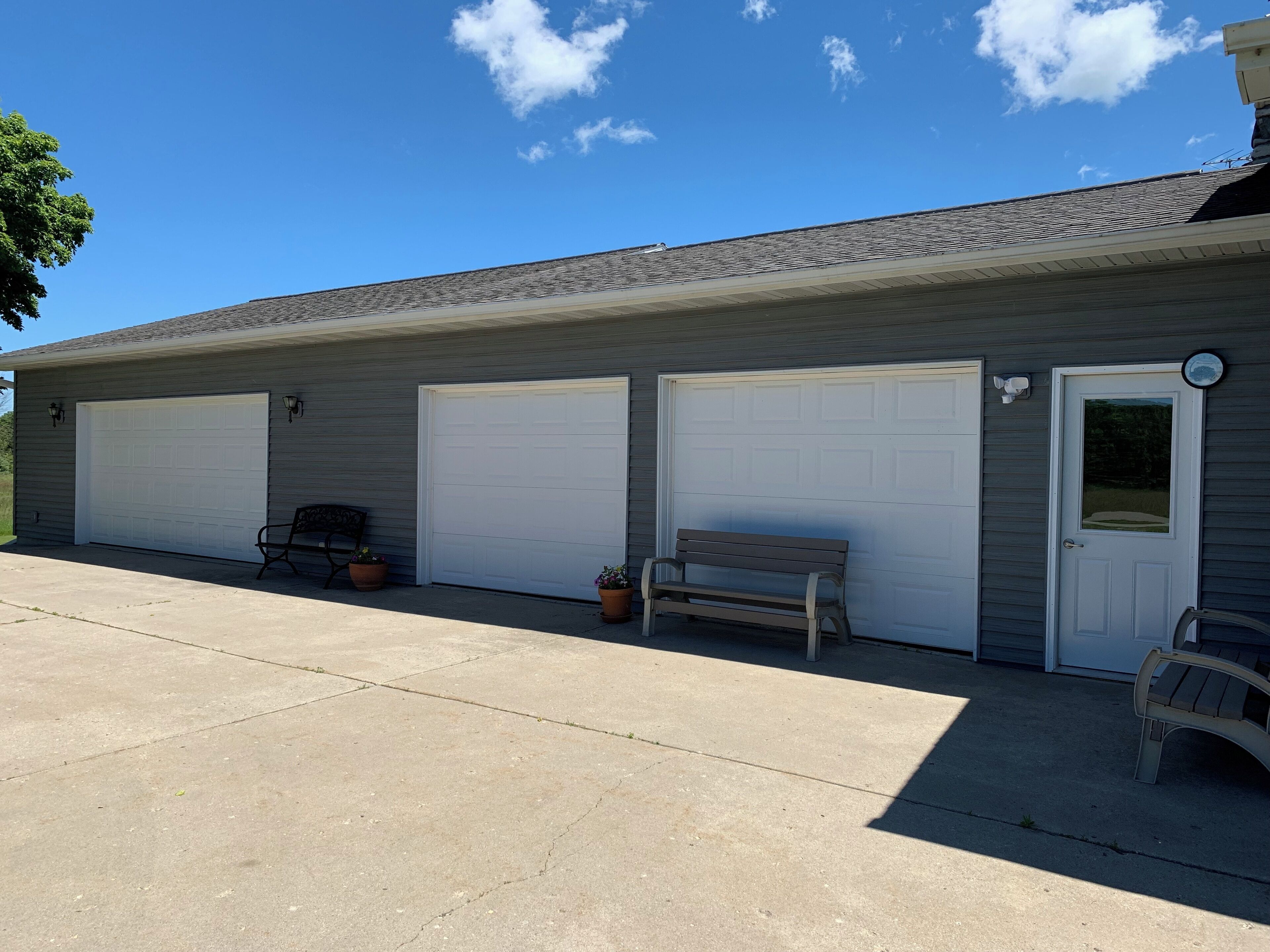 A two-story building with three garage doors, a bench, and two potted plants.