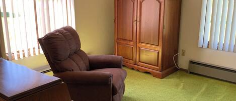 Ein Zimmer mit einem braunen Sessel, einem Holzschrank und einem grünen Teppich.