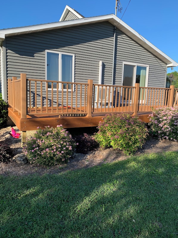 Une maison à deux étages dotée d’une terrasse en bois, d’un porche couvert et d’un jardin agrémenté de fleurs roses.
