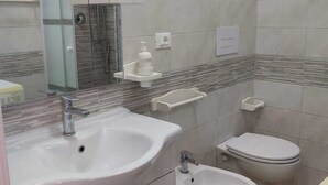 A modern bathroom with a large sink, bidet, toilet, and a glass-enclosed shower.