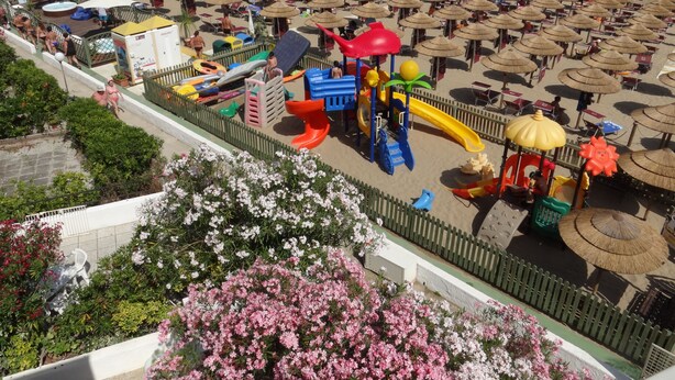 A beach with numerous umbrellas, a playground, and a view of the sea.