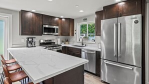 Une cuisine moderne avec des meubles en bois foncé, des appareils en acier inoxydable et un grand îlot central doté de tabourets de bar.