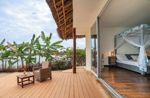 A bedroom with a canopy bed, a wooden deck with a thatched roof, and a view of palm trees and the sea. - Maharaja Boutique Hotel Zanzibar (Uroa)