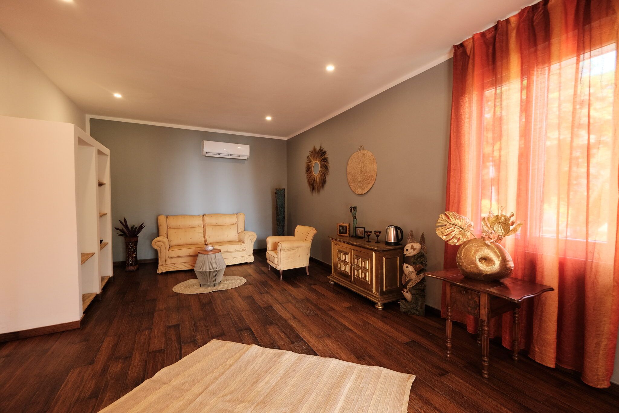 A living room with a sofa, armchairs, a coffee table, a cabinet with decorative items, and a large window with curtains.