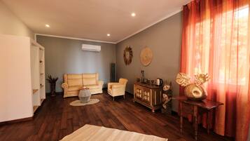 A living room with a sofa, armchairs, a coffee table, a cabinet with decorative items, and a large window with curtains.