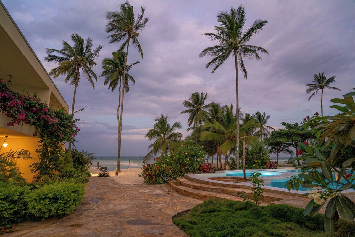 A pool area with palm trees, a beach, and a stone pathway leading to the beach.