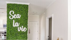 A hallway with a green wall featuring the text "Sea la vie" and a wooden cabinet with a vase and basket. - Amazing vacation rental, great location,pool,close to the beach and golf course  (Myrtle Beach)