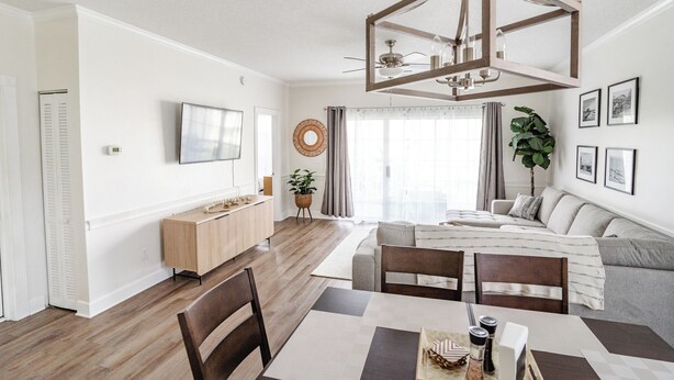 A modern living room with a dining area, a large window with curtains, a ceiling fan, and a mounted TV. - Amazing vacation rental, great location,pool,close to the beach and golf course  (Myrtle Beach)
