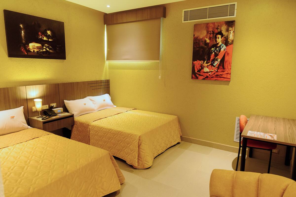 A hotel room with two beds, a desk, a chair, and artwork on the walls.