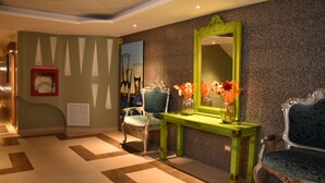 A lobby with a green console table, two blue upholstered chairs, a large mirror, and a wall-mounted vase with flowers. - NP Hotel & Suites (Guayaquil)