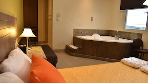 A hotel room with a bed, a small table with a lamp, a sofa, a large bathtub, and a window. - NP Hotel & Suites (Guayaquil)