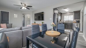 Een moderne woonkamer met een hoekbank, een eettafel met stoelen, een plafondventilator en een keuken met kasten en een aanrecht.