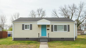 Een gelijkvloers huis met een veranda, een blauwe deur en een kleine voortuin.
