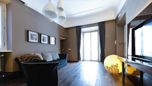 Una sala moderna con piso de madera oscura, un sofá negro con cojines, un ventanal con cortinas y una lámpara esférica original.