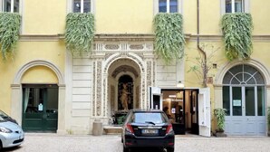 Un edificio con fachada amarilla, una entrada central con un arco decorativo y dos plantas colgantes verdes.