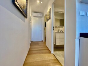 A narrow hallway with wooden flooring leading to a bathroom with a white sink and mirror.
