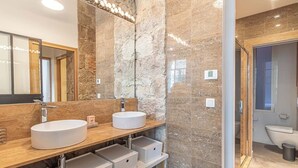 Un baño moderno con dos lavamanos, un espejo grande y una pared de piedra.