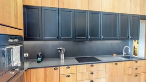 A modern kitchen with wooden cabinets, a black backsplash, stainless steel appliances, and a built-in sink. - Elegant Belle Époque Apartment in Central Menton (Menton)