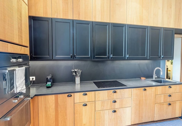 Eine moderne Küche mit Holzausstattung, einer schwarzen Spritzschutzwand, Edelstahlgeräten und einer integrierten Spüle.