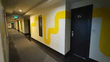 A hallway with a modern design, featuring a large yellow and white abstract wall art, a black door with a number, and a clean, well-lit environment.