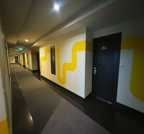 Un couloir au design moderne, agrémenté d’une grande œuvre d’art abstraite aux couleurs jaune et blanche, d’une porte noire portant un numéro et d’un environnement propre et bien éclairé.