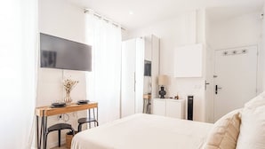 Une chambre d’hôtel moderne dotée d’un grand lit, d’un bureau agrémenté d’un vase de fleurs, d’une télévision à écran plat et d’une armoire.