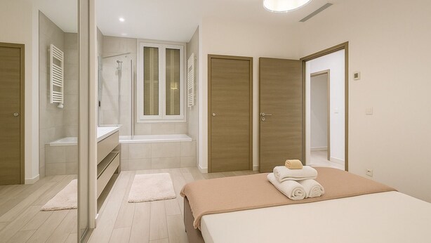 Een moderne slaapkamer met een groot bed, een inloopkast, een badkamer met douche en een raam met luiken.