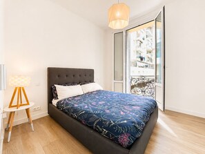 Un dormitorio con cama, lámpara de noche y vistas a un balcón.