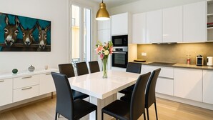 A modern kitchen with white cabinets, a dining table with chairs, and a pendant light.