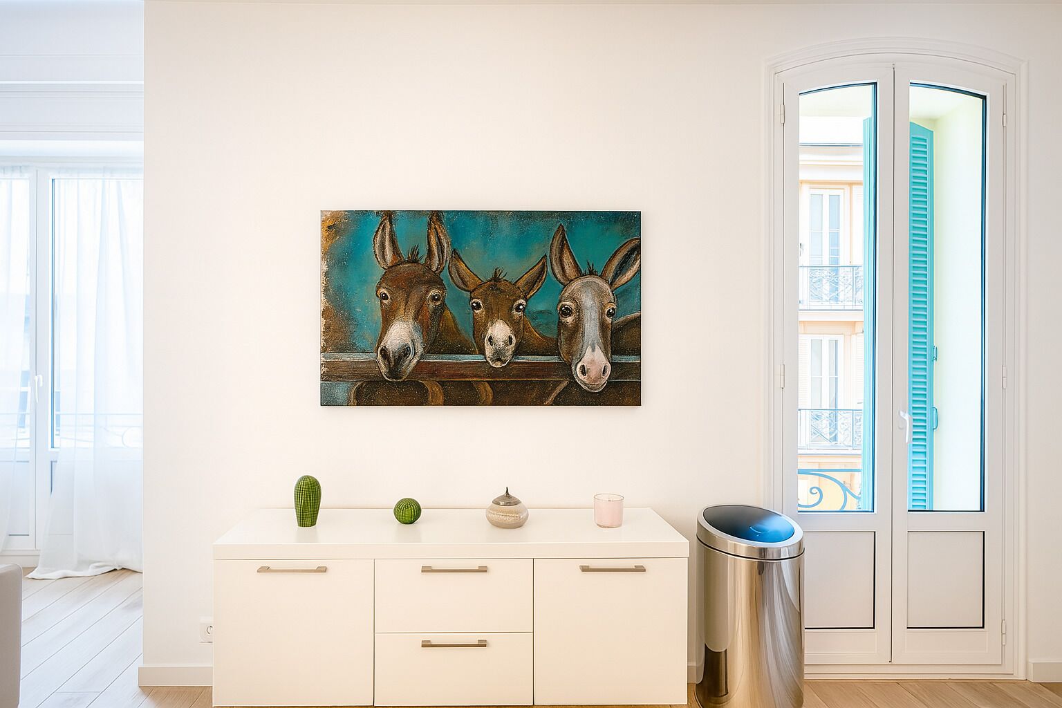 A room with a white cabinet, a trash bin, and a painting of donkeys on the wall.