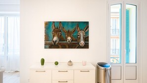 Een kamer met een wit kastje, een prullenbak en een schilderij van ezels aan de muur.