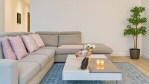 Een moderne woonkamer met een grijze bank, een witte salontafel en een potplant.